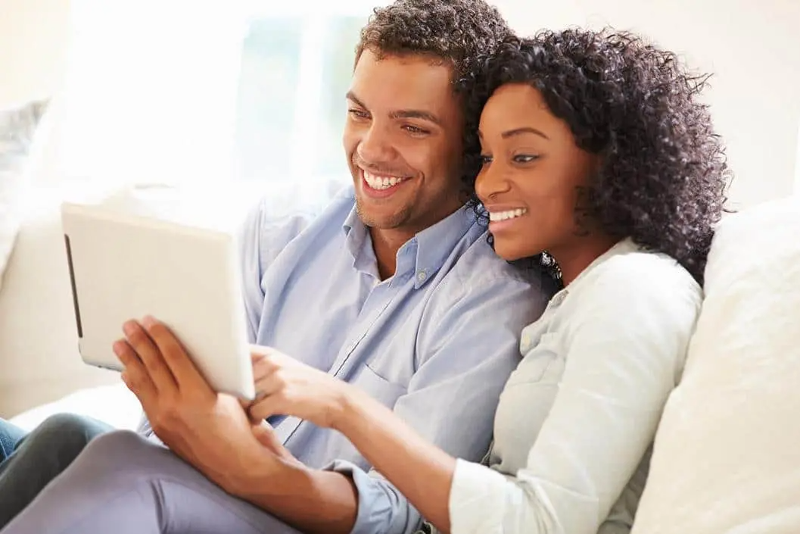 Couple sitting on white couch browsing flooring products online.